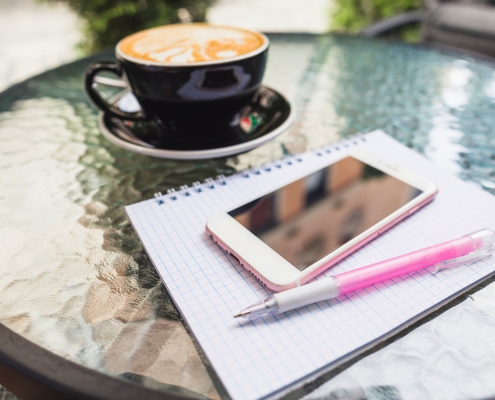 tavolo con penna, quaderno, cellulare e cappuccino sullo sfondo