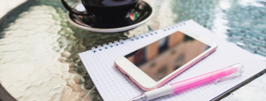 tavolo con penna, quaderno, cellulare e cappuccino sullo sfondo